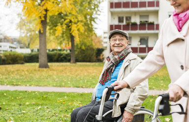 Senior woman with wheeled walker and senior man in wheelchair outdoors in autumn - UUF006125