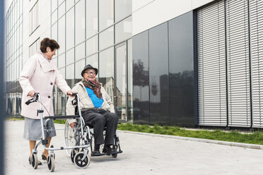 Senior woman with wheeled walker and senior man in wheelchair on pavement - UUF006132