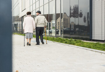 Senior couple walking with walking sticks on pavement - UUF006133