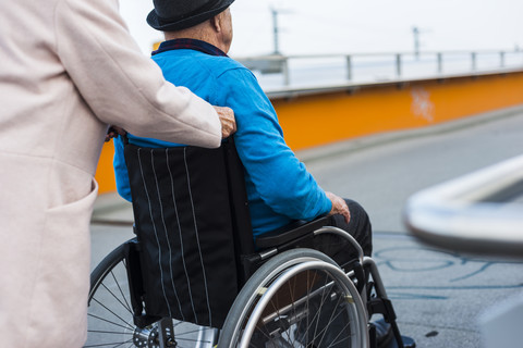 Ältere Frau schiebt ihren Mann im Rollstuhl, lizenzfreies Stockfoto