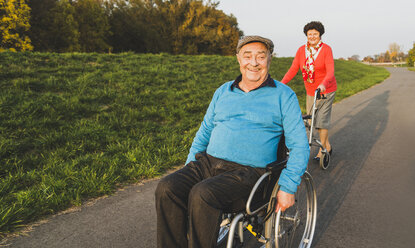 Lächelndes Seniorenpaar mit Rollstuhl und Rollator auf einem Weg - UUF006153