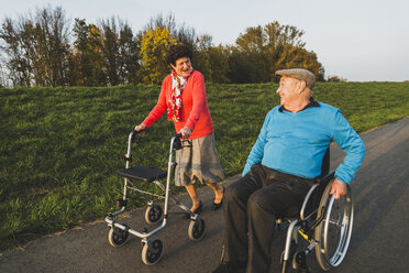 Lächelndes Seniorenpaar mit Rollstuhl und Rollator auf einem Weg - UUF006154