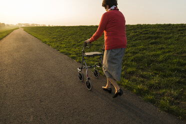 Senior woman walking with wheeled walker on a path - UUF006155