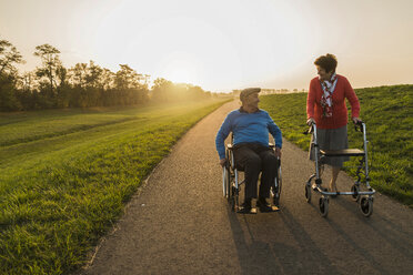 Lächelndes Seniorenpaar mit Rollstuhl und Rollator auf einem Weg - UUF006156