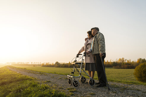 Senior couple with walking stick and wheeled walker standing in the nature - UUF006158