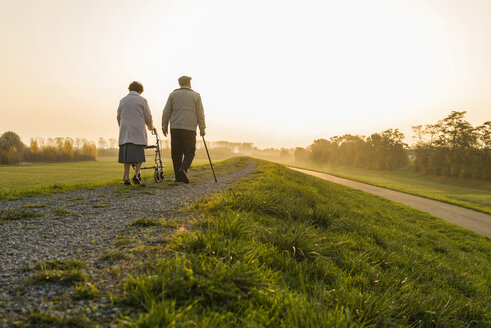 Senior couple walking with walking stick and wheeled walker in the nature - UUF006160