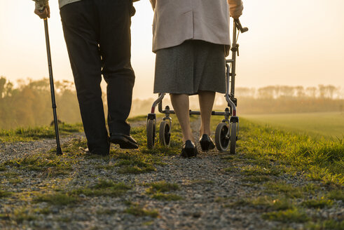 Senior couple walking with walking stick and wheeled walker in the nature - UUF006161