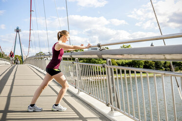 Deutschland, Frankfurt, junger Sportler beim Dehnen auf der Brücke - PUF000436