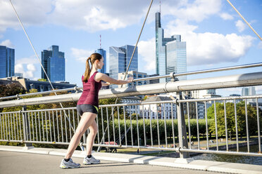 Germany, Frankfurt, young athlete stretching on bridge - PUF000438