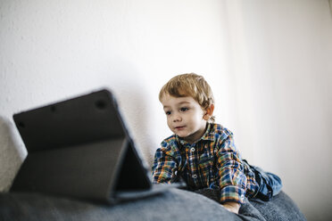 Porträt eines kleinen Jungen, der auf der Rückenlehne einer Couch liegt und auf ein digitales Tablet schaut - JRFF000201