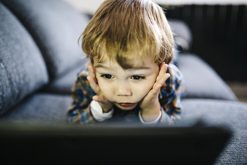 Portrait of little boy lying on the couch looking at digital tablet - JRFF000203