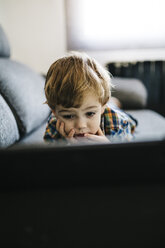 Porträt eines kleinen Jungen, der auf der Couch liegt und auf ein digitales Tablet schaut - JRFF000204