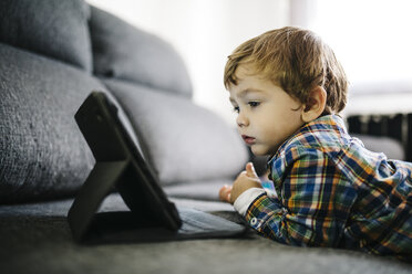 Portrait of little boy lying on the couch looking at digital tablet - JRFF000208