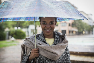 Italien, Grado, Porträt einer lächelnden Frau mit Regenschirm an einem regnerischen Tag - MAUF000058