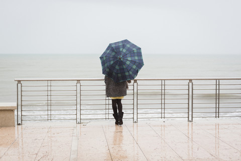 Italien, Grado, Rückenansicht einer Frau mit Regenschirm und Blick auf das Meer, lizenzfreies Stockfoto