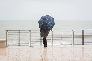 Italien, Grado, Rückenansicht einer Frau mit Regenschirm und Blick auf das Meer - MAUF000064