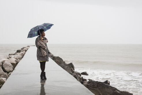 Italien, Grado, Frau mit Regenschirm an einem regnerischen Tag mit Blick auf das Meer - MAUF000066