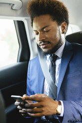 Businessman sitting on back seat of a car looking at smartphone - EBSF001140