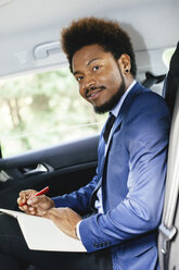 Porträt eines Geschäftsmannes, der auf dem Rücksitz eines Autos sitzt und etwas aufschreibt - EBSF001144