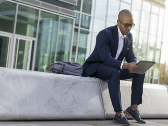 Deutschland, Köln, Junger Geschäftsmann auf Bank sitzend, mit digitalem Tablet - MADF000684