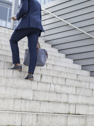 Deutschland, Köln, Junger Geschäftsmann, der sein Smartphone überprüft, beim Treppensteigen - MADF000695