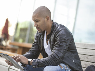 Germany, Cologne, Young man sitting on bench using digital tablet - MADF000699