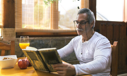 Mann sitzt am Frühstückstisch und liest ein Buch - MGOF001088