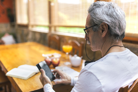 Mann sitzt am Frühstückstisch und benutzt sein Smartphone, lizenzfreies Stockfoto