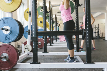 Woman lifting barbell in a power rack - MADF000710