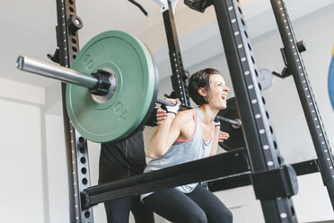 Two women doing barbell squats in a power rack - MADF000735