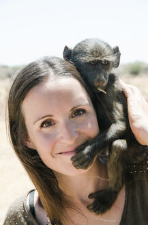 Namibia, Porträt einer lächelnden Frau mit Pavianbaby auf der Schulter - GEMF000502