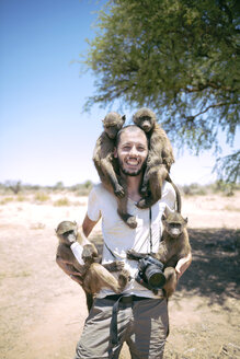 Namibia, man with camera holding four baby baboons - GEMF000505