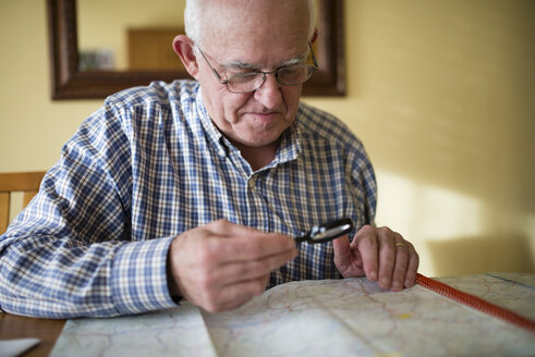 Älterer Mann betrachtet eine Straßenkarte mit Lupe - RAE000681