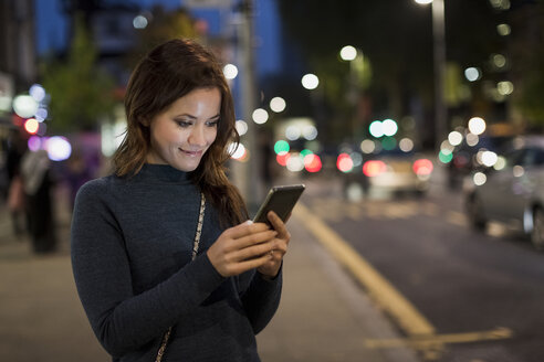 Frau überprüft ihr Smartphone am Straßenrand - MAUF000095