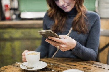 Frau überprüft ihr Smartphone in einem Café - MAUF000097