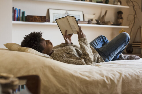 Junge Frau liegt auf dem Bett und liest ein Buch - MAUF000109