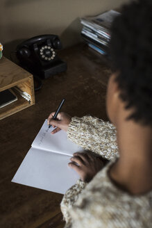 Junge Frau am Schreibtisch schreibt in ein Notizbuch - MAUF000118