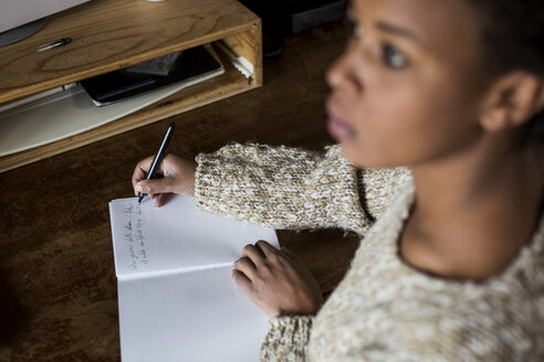 Junge Frau am Schreibtisch schreibt in ein Notizbuch - MAUF000120