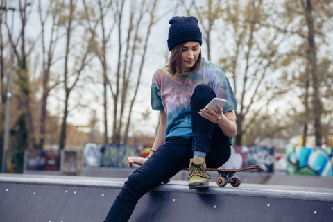 Junge Frau im Skatepark schaut auf ihr Handy, lizenzfreies Stockfoto