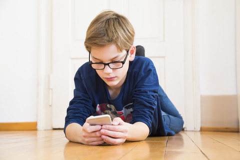 Junge liegt auf dem Boden und schaut auf sein Smartphone, lizenzfreies Stockfoto