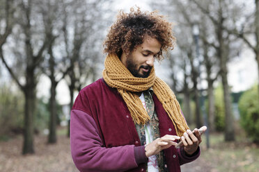 Porträt eines Mannes mit gefärbten Locken, der einen Schal trägt und sein Smartphone benutzt - GDF000904