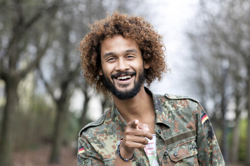 Portrait of smiling man with dyed ringlets wearing camouflage shirt pointing on viewer - GDF000906