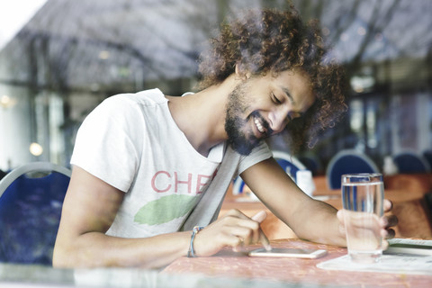 Porträt eines lächelnden Mannes, der in einem Café sitzt und ein Smartphone benutzt, lizenzfreies Stockfoto