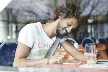 Porträt eines lächelnden Mannes, der in einem Café sitzt und ein Smartphone benutzt - GDF000908