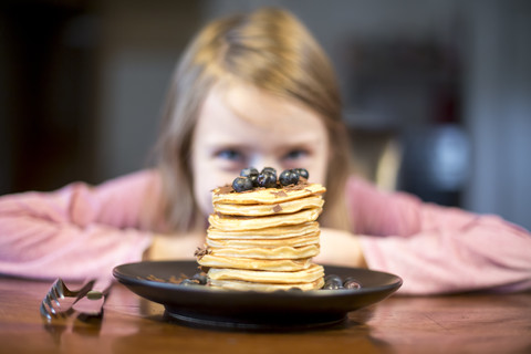 Teller mit Stapel von Pfannkuchen mit kleinem Mädchen im Hintergrund, lizenzfreies Stockfoto