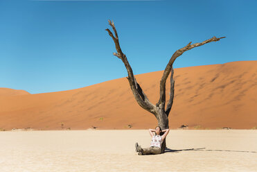 Namibia, Namib-Wüste, Frau ruht sich an totem Baum in Deadvlei aus - GEMF000515