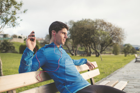 Athlete sitting on bench after training listening to music from smartphone stock photo