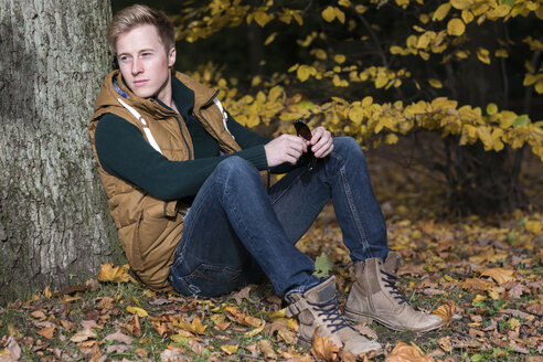 Young man sitting at tree in autumn - GDF000921