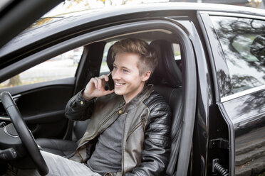 Smiling young man in car on cell phone - GDF000931