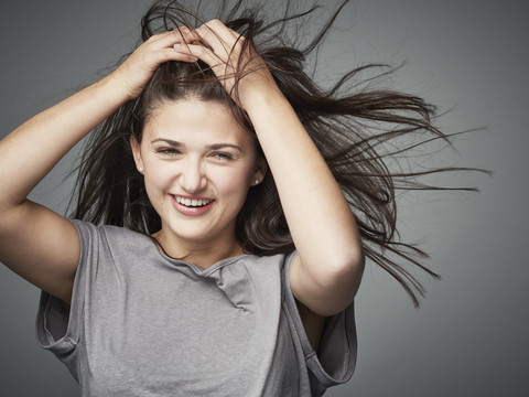 Porträt einer glücklichen brünetten jungen Frau mit Händen im Haar, lizenzfreies Stockfoto